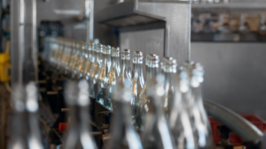 Rows of clear glass bottles moving along a conveyor belt in a manufacturing facility.